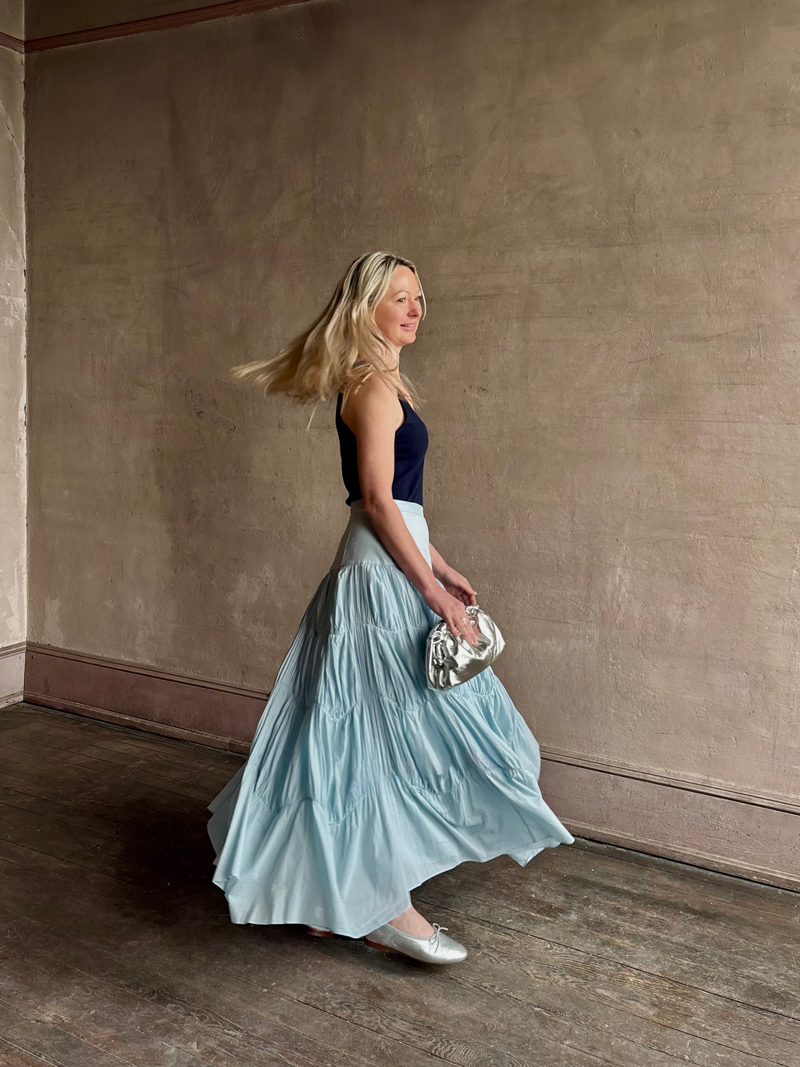 Mature woman wearing Davina Drop Waist Maxi Skirt from Ulla Johnson  rendered in Adriatic Blue hue with intricate full skirt ruching