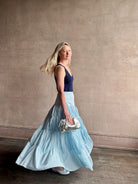 Mature woman wearing Davina Drop Waist Maxi Skirt from Ulla Johnson  rendered in Adriatic Blue hue with intricate full skirt ruching