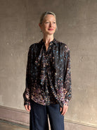 woman wearing designer Ulla Johnson long-sleeve black silk blouse subtle floral print collared button front ruffle