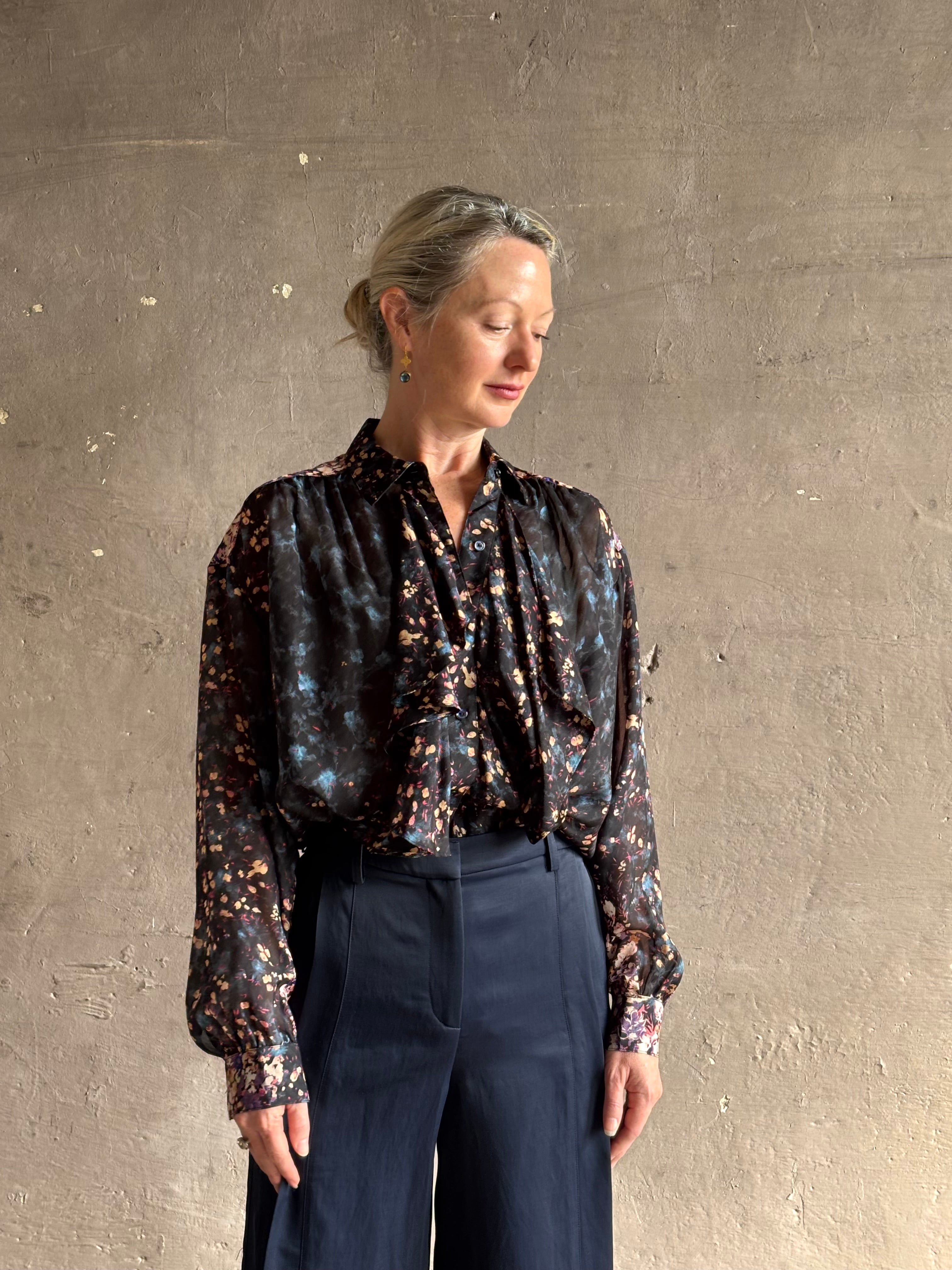 woman wearing designer Ulla Johnson long-sleeve black silk blouse subtle floral print collared button front ruffle detail
