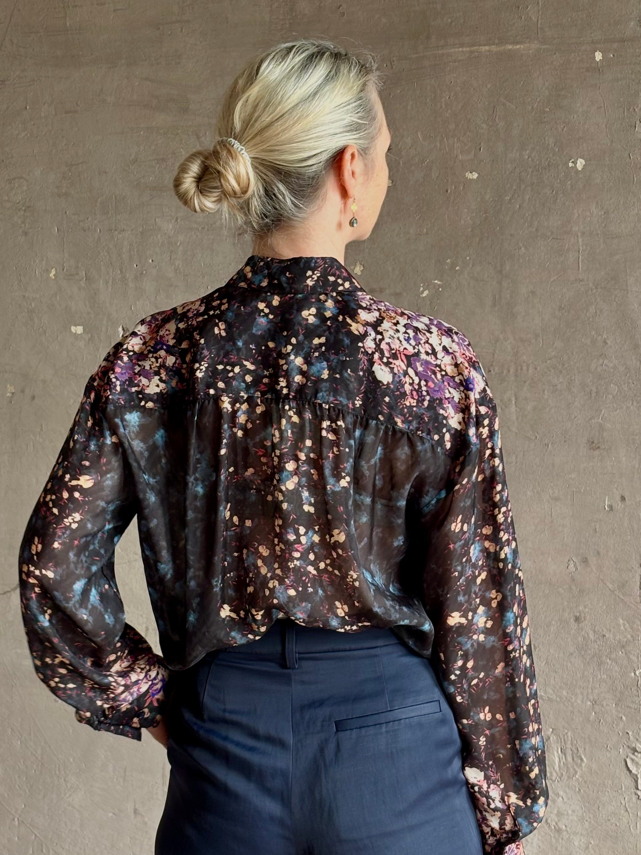 woman wearing Ulla Johnson long-sleeve black silk blouse subtle floral print collared button front ruffle detail