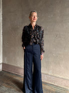 woman wearing Ulla Johnson long-sleeve black silk blouse subtle floral print collared button front ruffle detail
