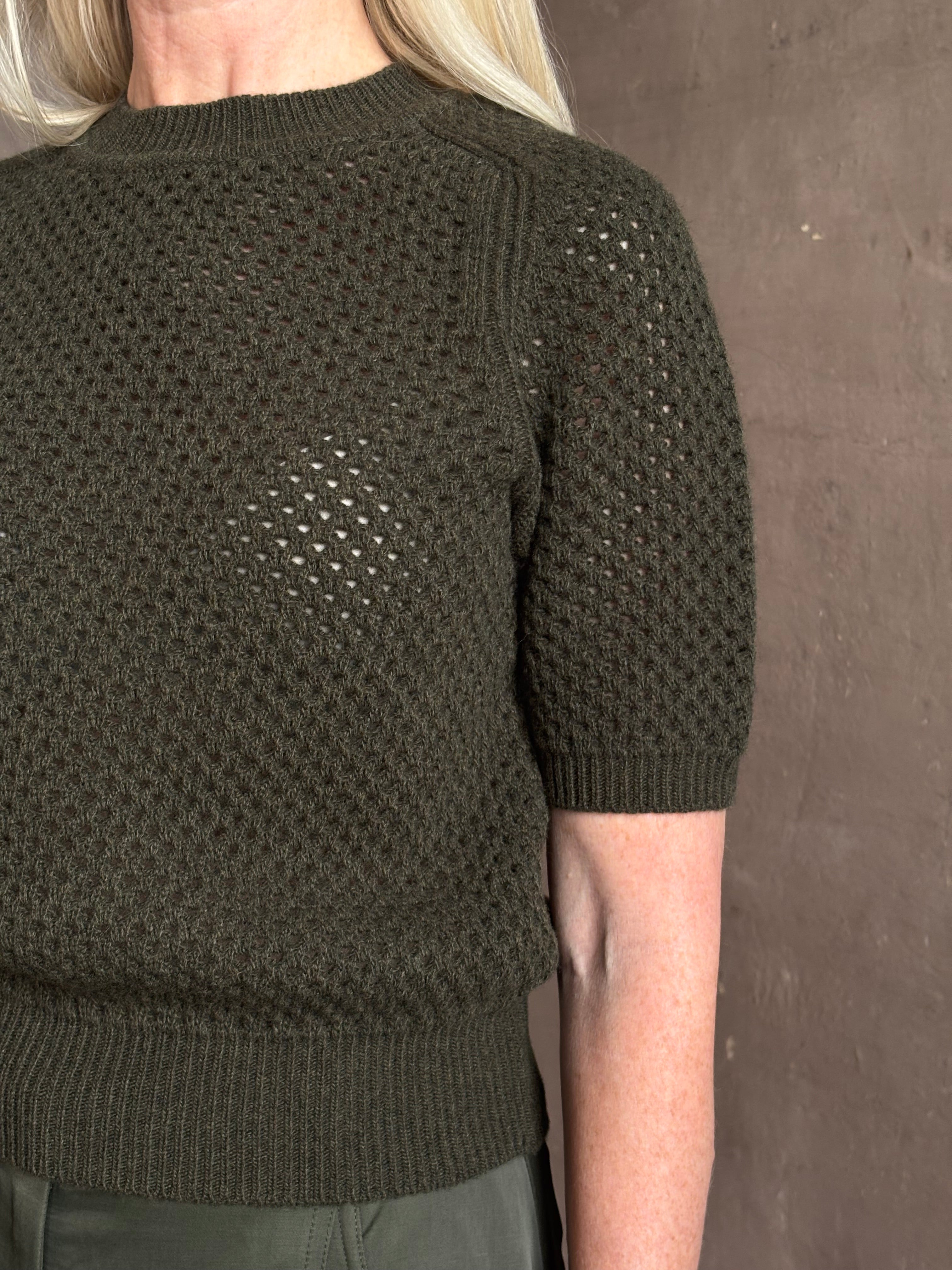 Mature woman wearing designer Ulla Johnson Imara Short Sleeve dark green Sweater with a dimensional open weave