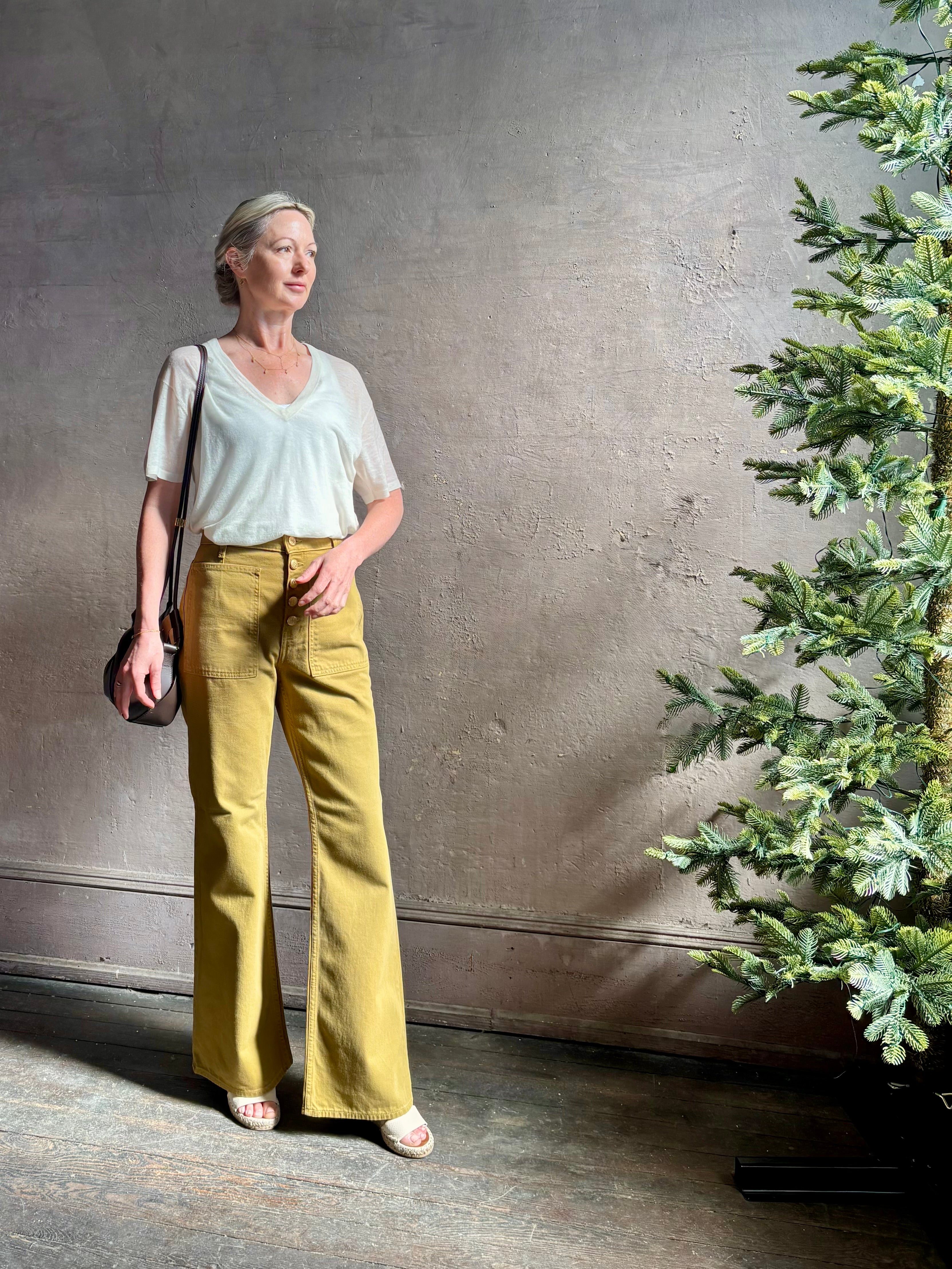 Mature woman wearing luxury Ulla Johnson Lou cotton rigid full length green denim with gold button fly patch pocket
