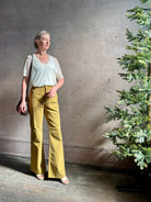 Mature woman wearing luxury Ulla Johnson Lou cotton rigid full length green denim with gold button fly patch pocket