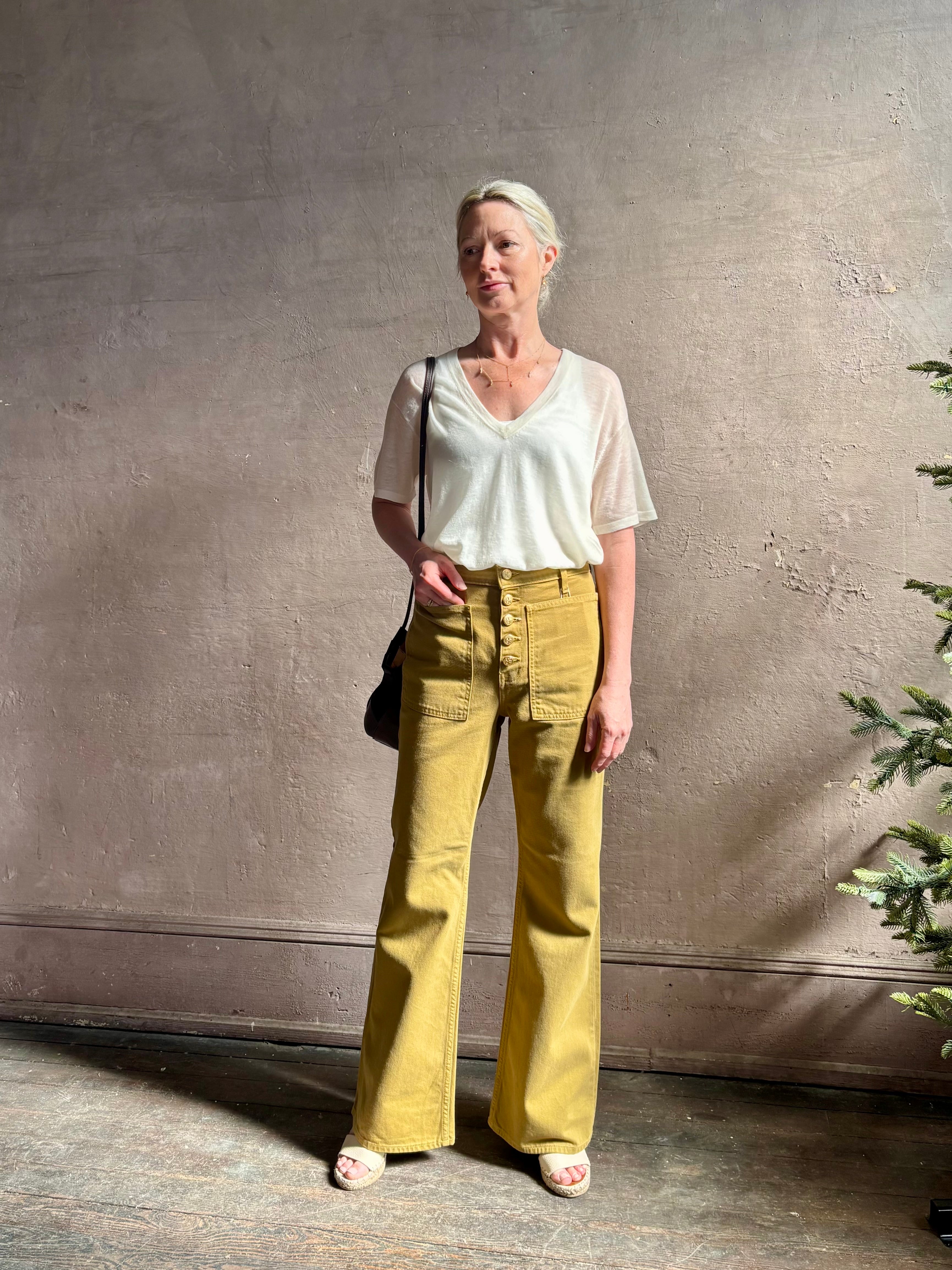 Mature woman wearing luxury Ulla Johnson Lou cotton rigid full length green denim with gold button fly patch pocket