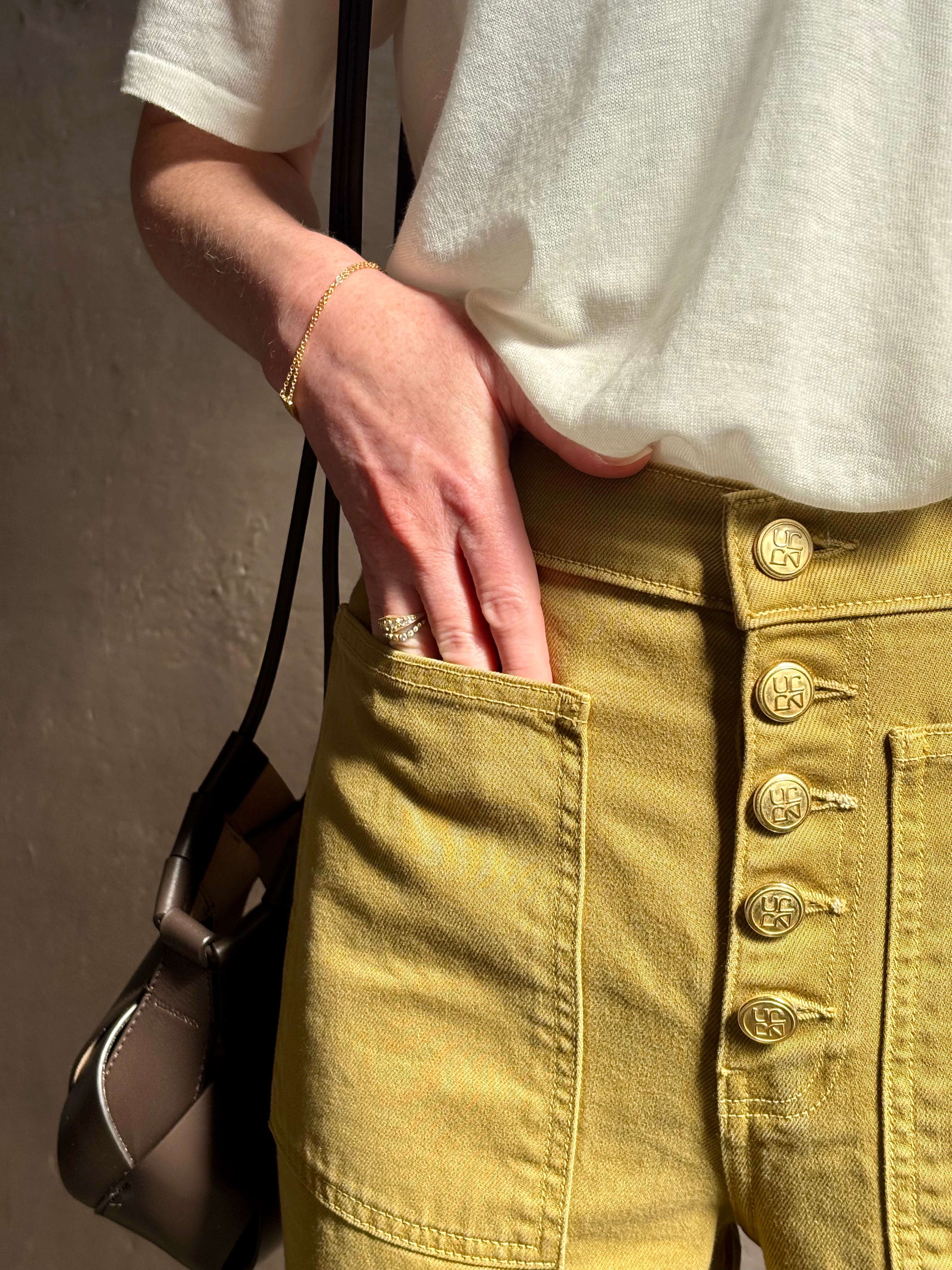 Mature woman wearing luxury Ulla Johnson Lou cotton rigid full length green denim with gold button fly patch pocket