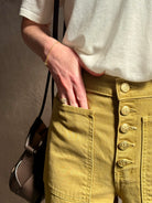 Mature woman wearing luxury Ulla Johnson Lou cotton rigid full length green denim with gold button fly patch pocket
