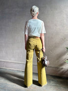Mature woman wearing luxury Ulla Johnson Lou cotton rigid full length green denim with gold button fly patch pocket