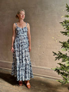Mature woman wearing Ophelia Cami Cotton maxi Dress from Ulla Johnson rendered in a crisp white ground adorned with a soft black and light blue print and crafted from a cotton and viscose blend with an empire waist, sweatheart neckline and spaghetti straps