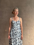 Mature woman wearing Ophelia Cami Cotton maxi Dress from Ulla Johnson rendered in a crisp white ground adorned with a soft black and light blue print and crafted from a cotton and viscose blend with an empire waist, sweatheart neckline and spaghetti straps