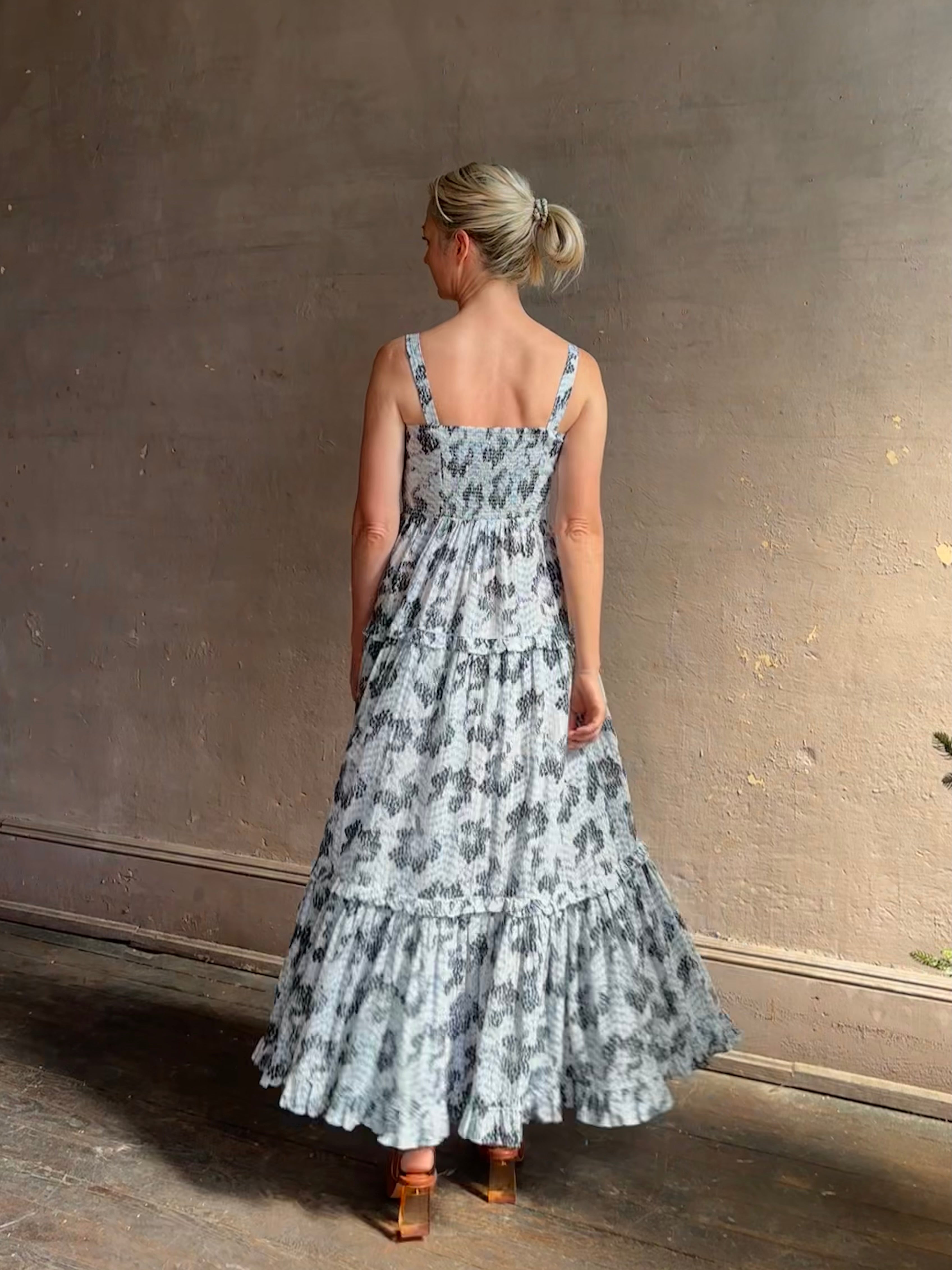 Mature woman wearing Ophelia Cami Cotton maxi Dress from Ulla Johnson rendered in a crisp white ground adorned with a soft black and light blue print and crafted from a cotton and viscose blend with an empire waist, sweatheart neckline and spaghetti straps