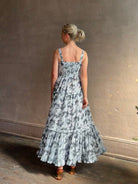 Mature woman wearing Ophelia Cami Cotton maxi Dress from Ulla Johnson rendered in a crisp white ground adorned with a soft black and light blue print and crafted from a cotton and viscose blend with an empire waist, sweatheart neckline and spaghetti straps
