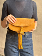 Mature woman with the luxury Italian leather  Paloma handbag with Tassel Flap from Ulla Johnson rendered in a rich caramel brown featuring a pull tassel magnetic snap closure and removable adjustable handle that seamlessly converts to a designer clutch