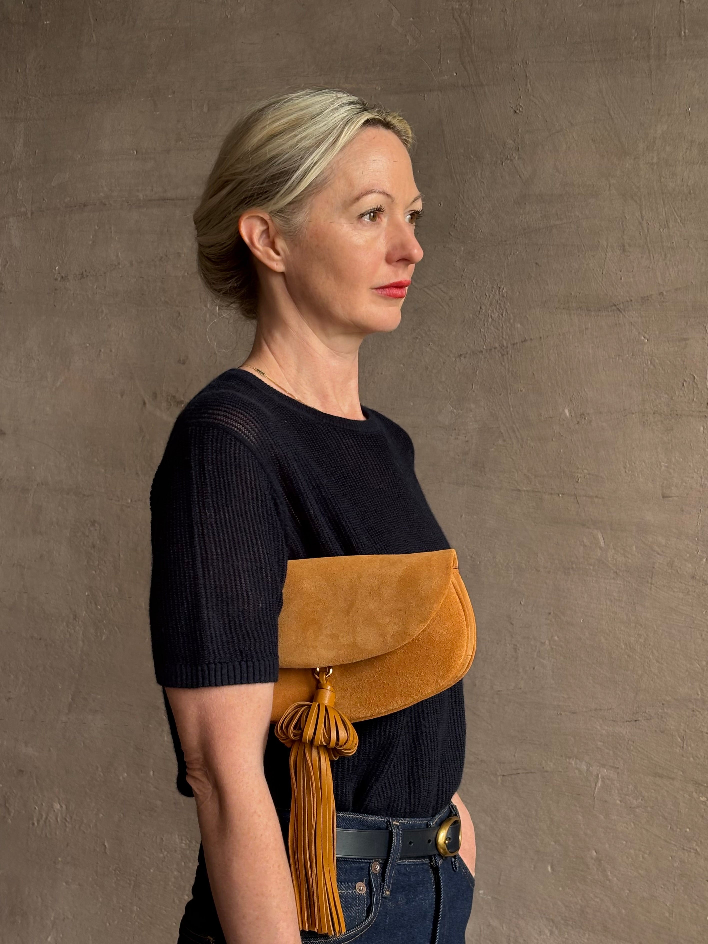 Mature woman with the luxury Italian leather  Paloma handbag with Tassel Flap from Ulla Johnson rendered in a rich caramel brown featuring a pull tassel magnetic snap closure and removable adjustable handle that seamlessly converts to a designer clutch