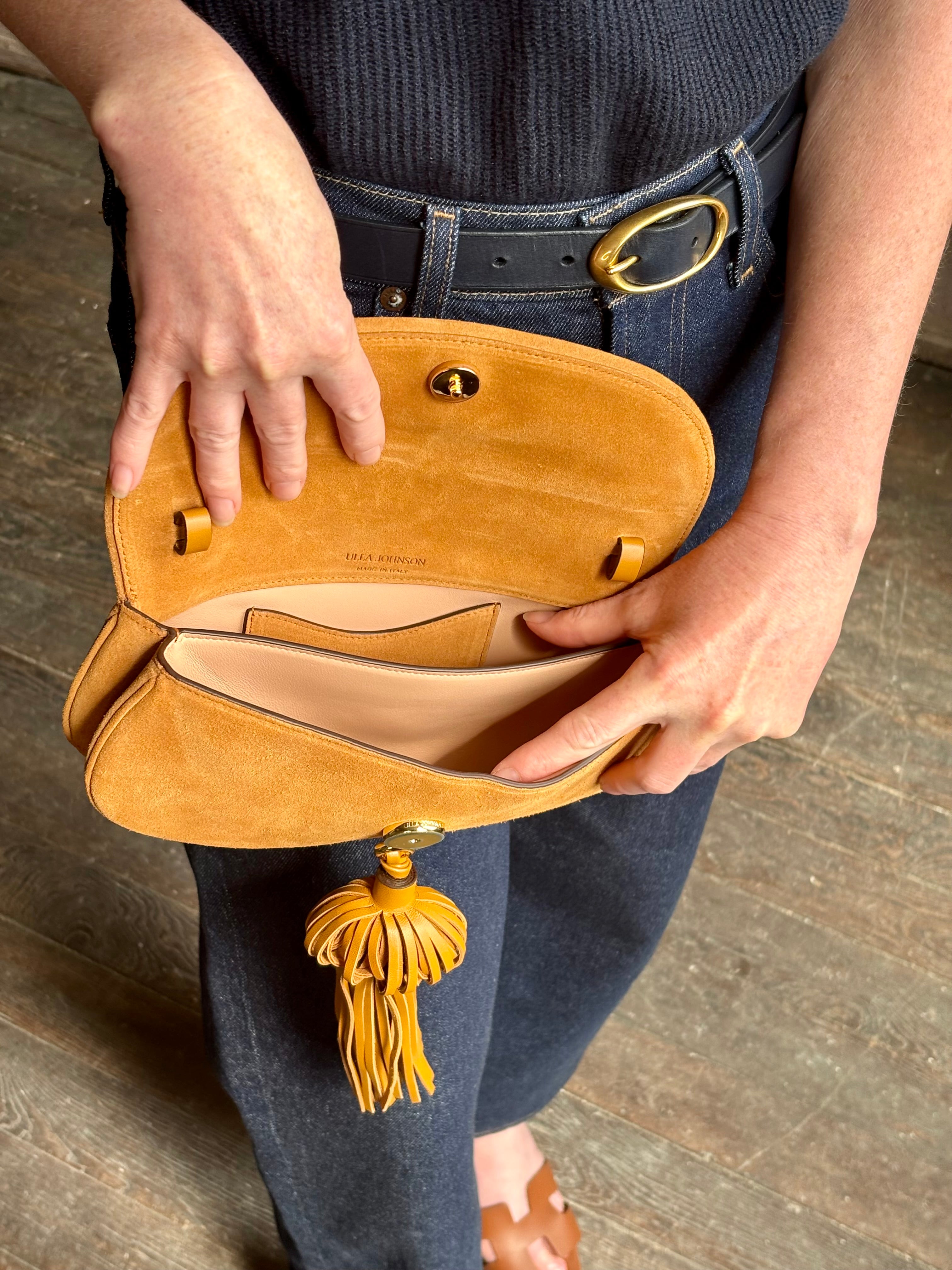 Mature woman with the luxury Italian leather  Paloma handbag with Tassel Flap from Ulla Johnson rendered in a rich caramel brown featuring a pull tassel magnetic snap closure and removable adjustable handle that seamlessly converts to a designer clutch