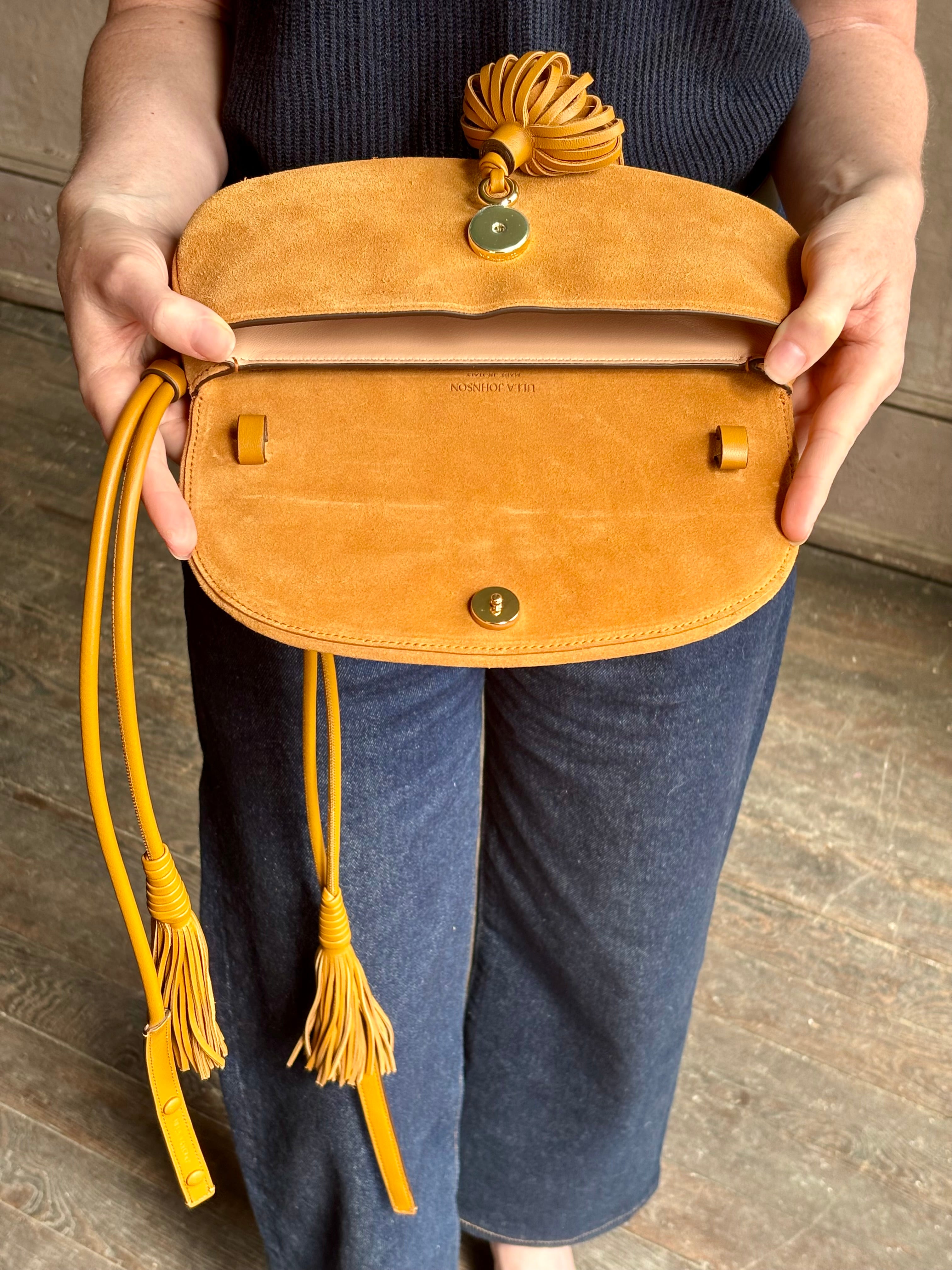 Mature woman with the luxury Italian leather  Paloma handbag with Tassel Flap from Ulla Johnson rendered in a rich caramel brown featuring a pull tassel magnetic snap closure and removable adjustable handle that seamlessly converts to a designer clutch