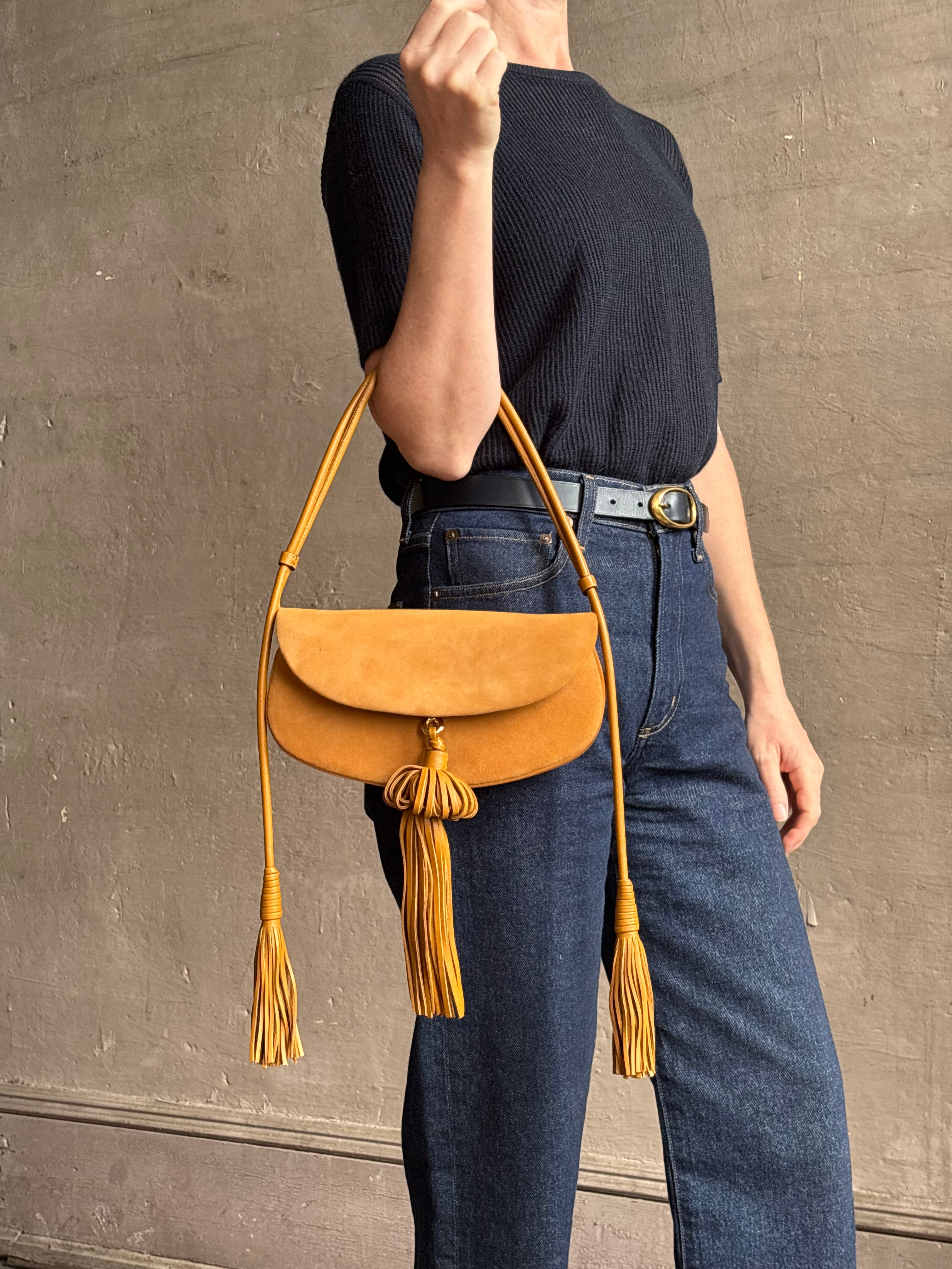 Mature woman with the luxury Italian leather  Paloma handbag with Tassel Flap from Ulla Johnson rendered in a rich caramel brown featuring a pull tassel magnetic snap closure and removable adjustable handle that seamlessly converts to a designer clutch