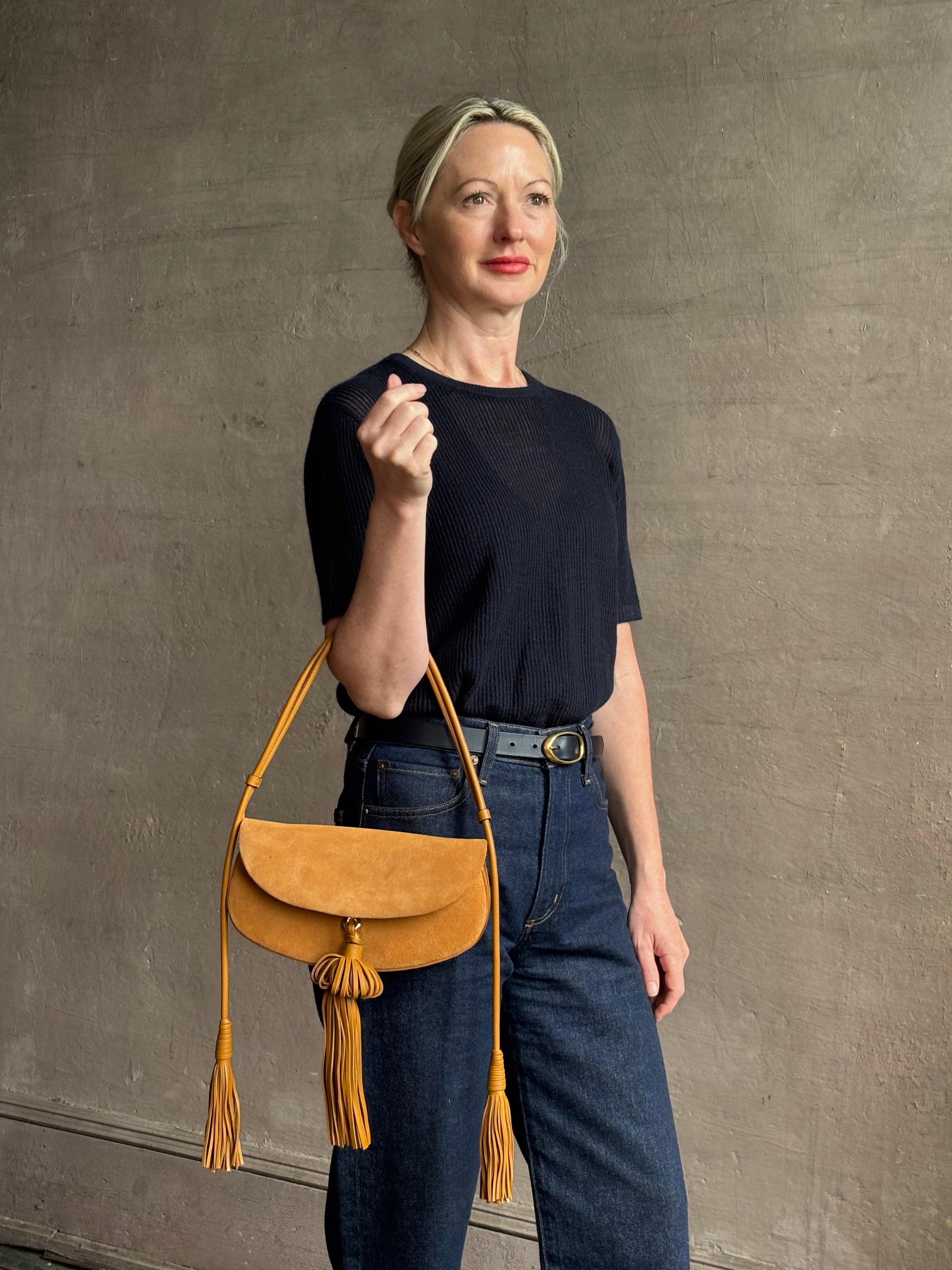 Mature woman with the luxury Italian leather  Paloma handbag with Tassel Flap from Ulla Johnson rendered in a rich caramel brown featuring a pull tassel magnetic snap closure and removable adjustable handle that seamlessly converts to a designer clutch