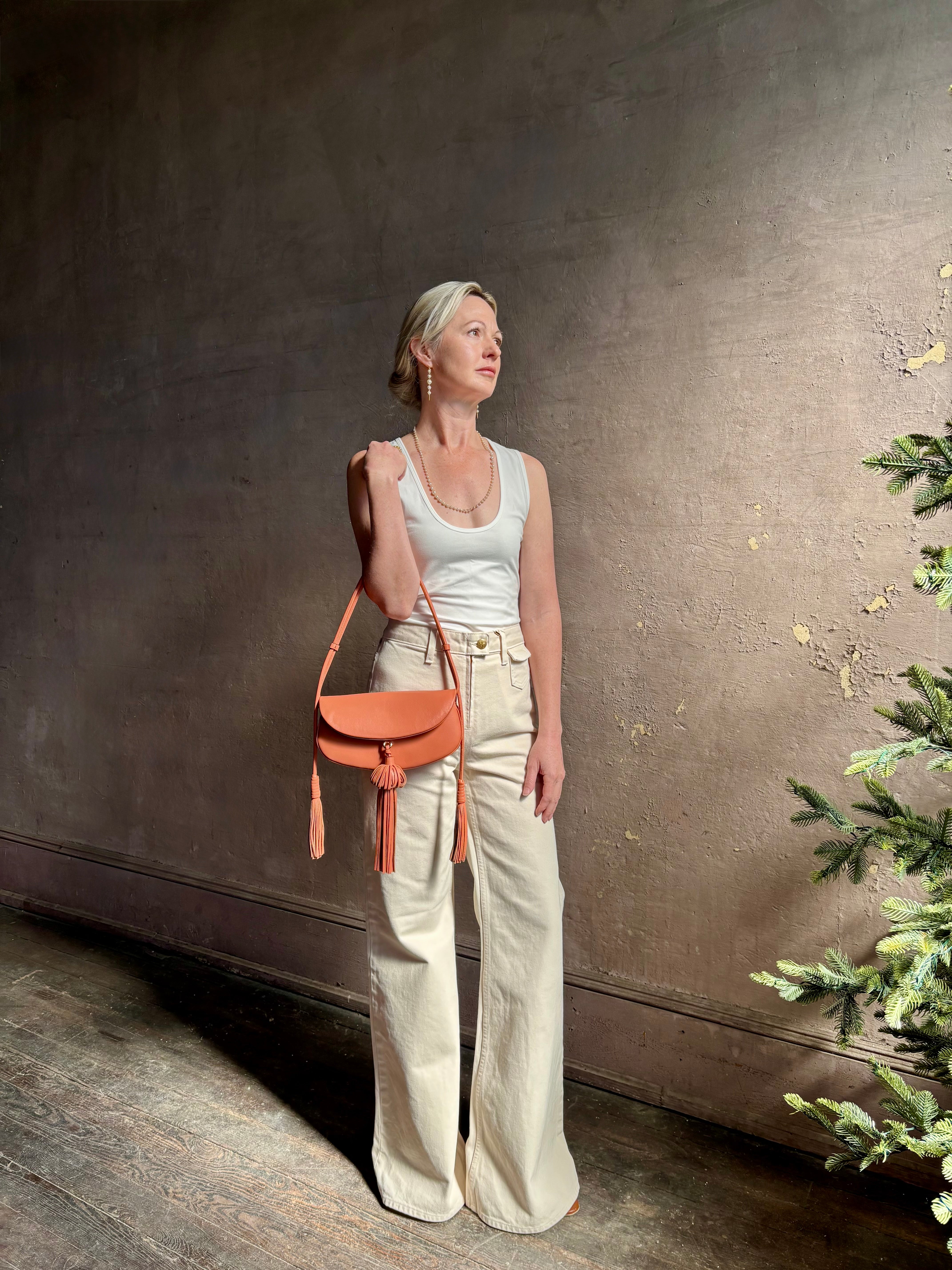 Mature woman with the luxury Italian leather  Paloma handbag with Tassel Flap from Ulla Johnson rendered in a warm pink featuring a pull tassel magnetic snap closure and removable adjustable handle that seamlessly converts to a designer clutch