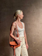 Mature woman with the luxury Italian leather  Paloma handbag with Tassel Flap from Ulla Johnson rendered in a warm pink featuring a pull tassel magnetic snap closure and removable adjustable handle that seamlessly converts to a designer clutch