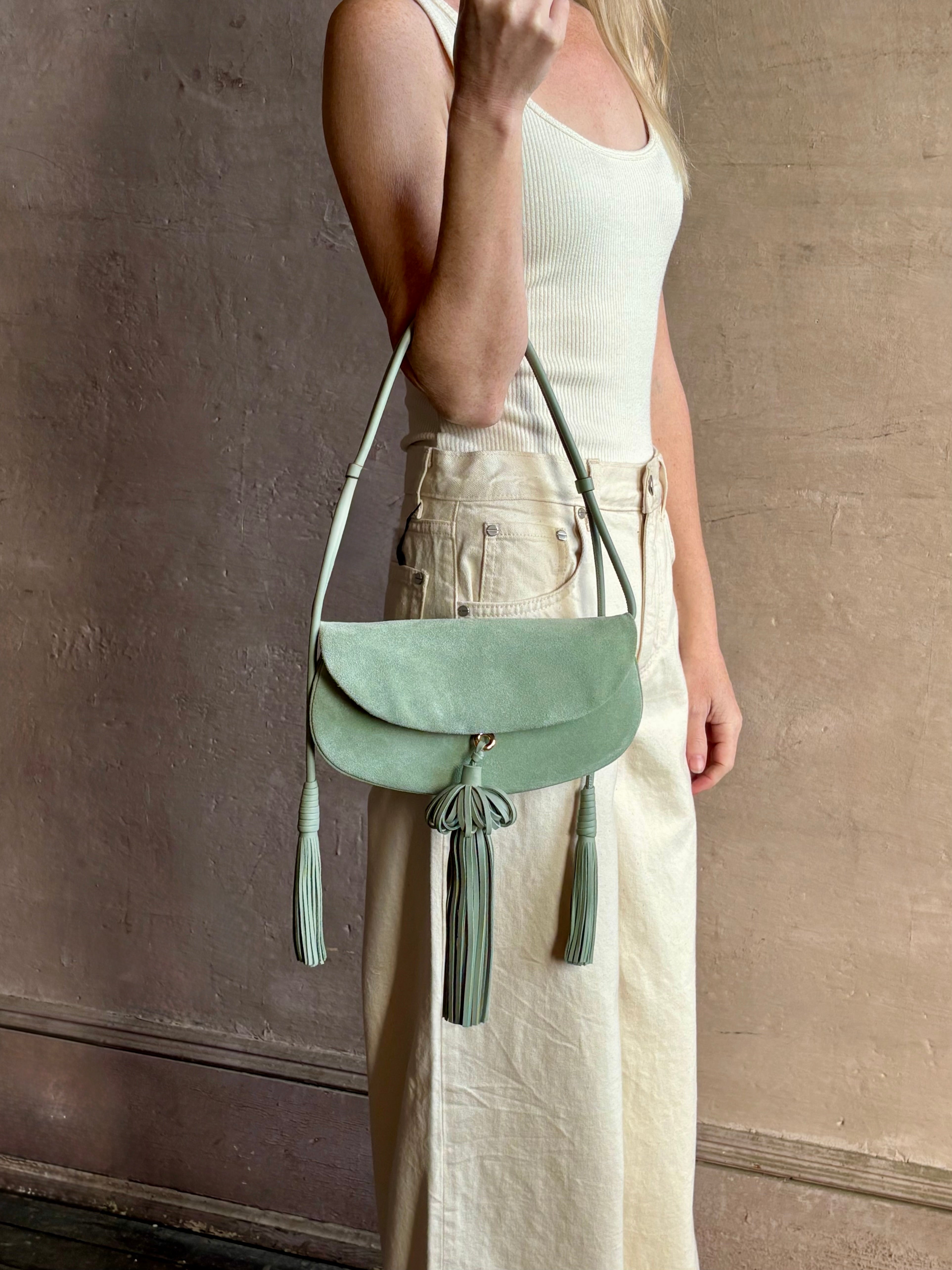 Image of woman holding premium suede leather ULLA JOHNSON Paloma Tassel Flap Bag in Sea Glass green with adjustable shoulder strap