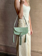 Image of woman holding premium suede leather ULLA JOHNSON Paloma Tassel Flap Bag in Sea Glass green with adjustable shoulder strap