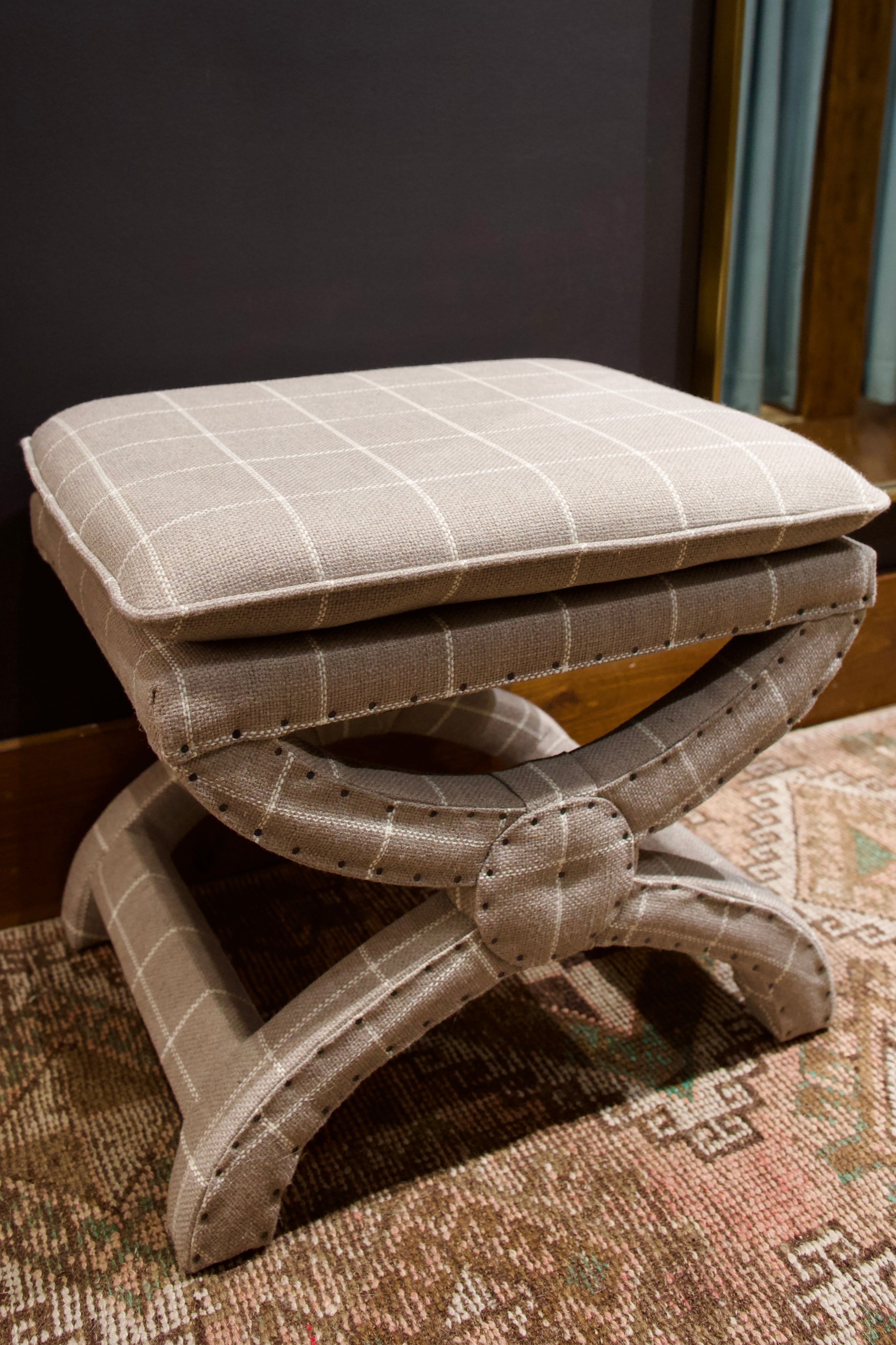 gray ottoman with a fixed pillow top seat cushion and a windowpane pattern fabric on a curved 'X' base 