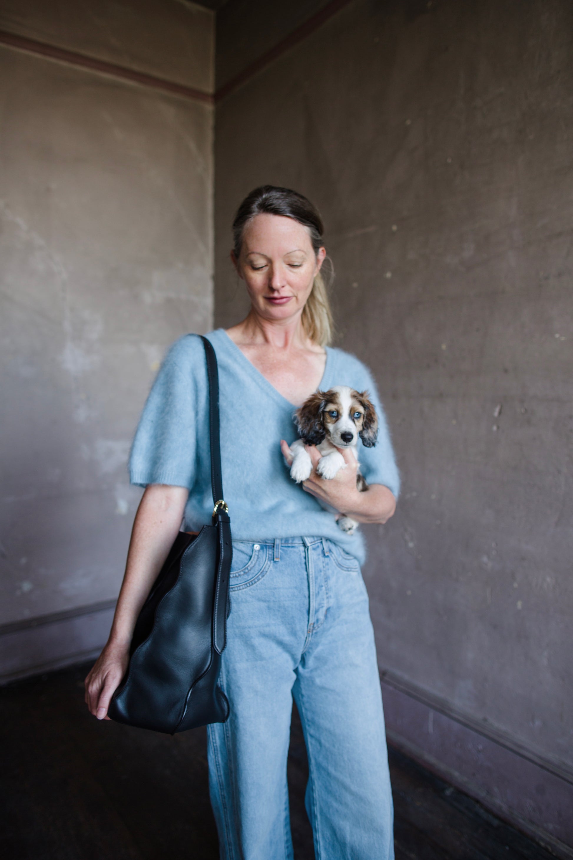 Image of a woman wearing the Adria Wave handbag by Ulla Johnson with curved seam detailing and a detachable snap pouch and adjustable strap.