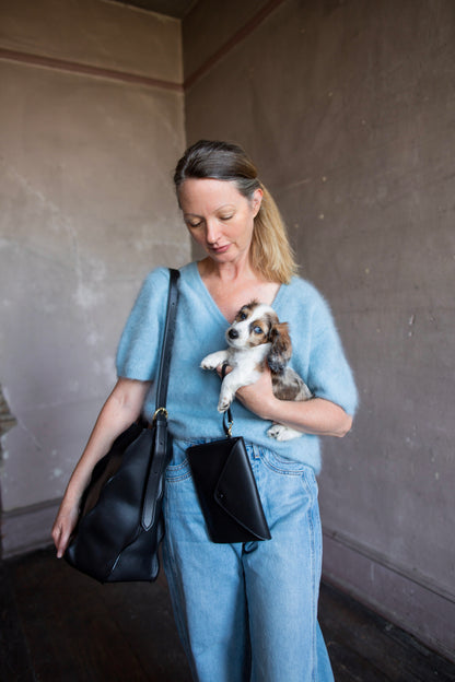 Image of a woman wearing the Adria Wave handbag by Ulla Johnson with curved seam detailing and a detachable snap pouch and adjustable strap.