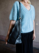 Image of a woman wearing the Adria Wave handbag by Ulla Johnson with curved seam detailing and a detachable snap pouch and adjustable strap.