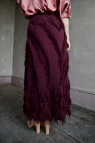 Mature model wearing a long burgundy skirt with a playful textured fringe Mature Woman wearing designer Ulla Johnson's Astrid Knit Maxi Skirt in Mahogany knit with fringe detailing 