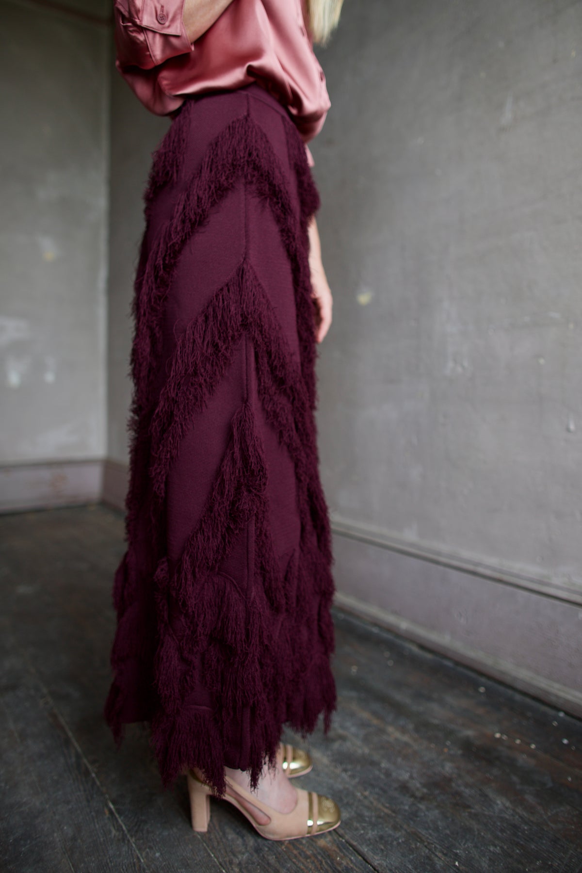 Mature Woman wearing designer Ulla Johnson's Astrid Knit Maxi Skirt in Mahogany knit with fringe detailing 