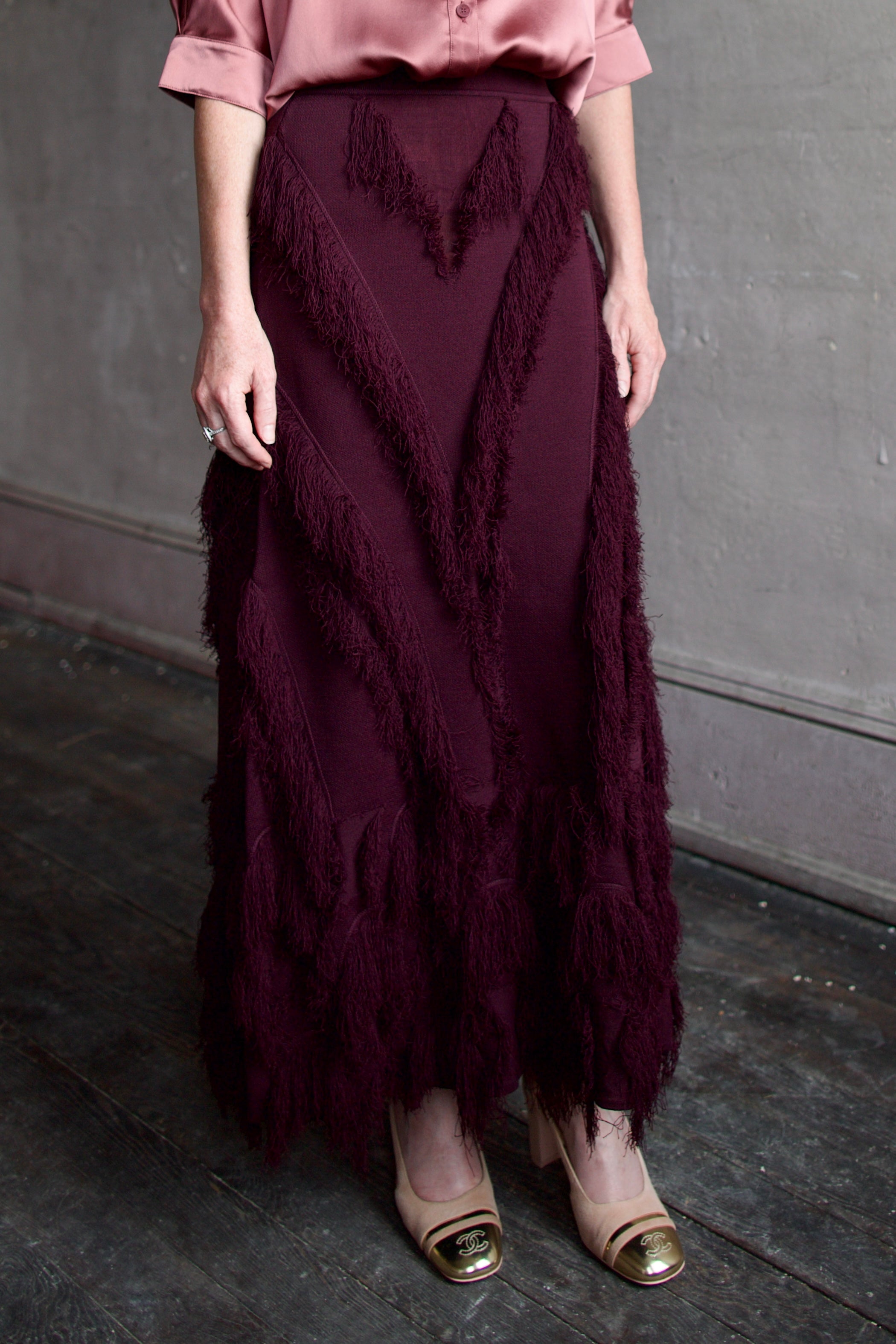 Mature model wearing a long burgundy skirt with a playful textured fringe pattern that can easily be dressed up or down