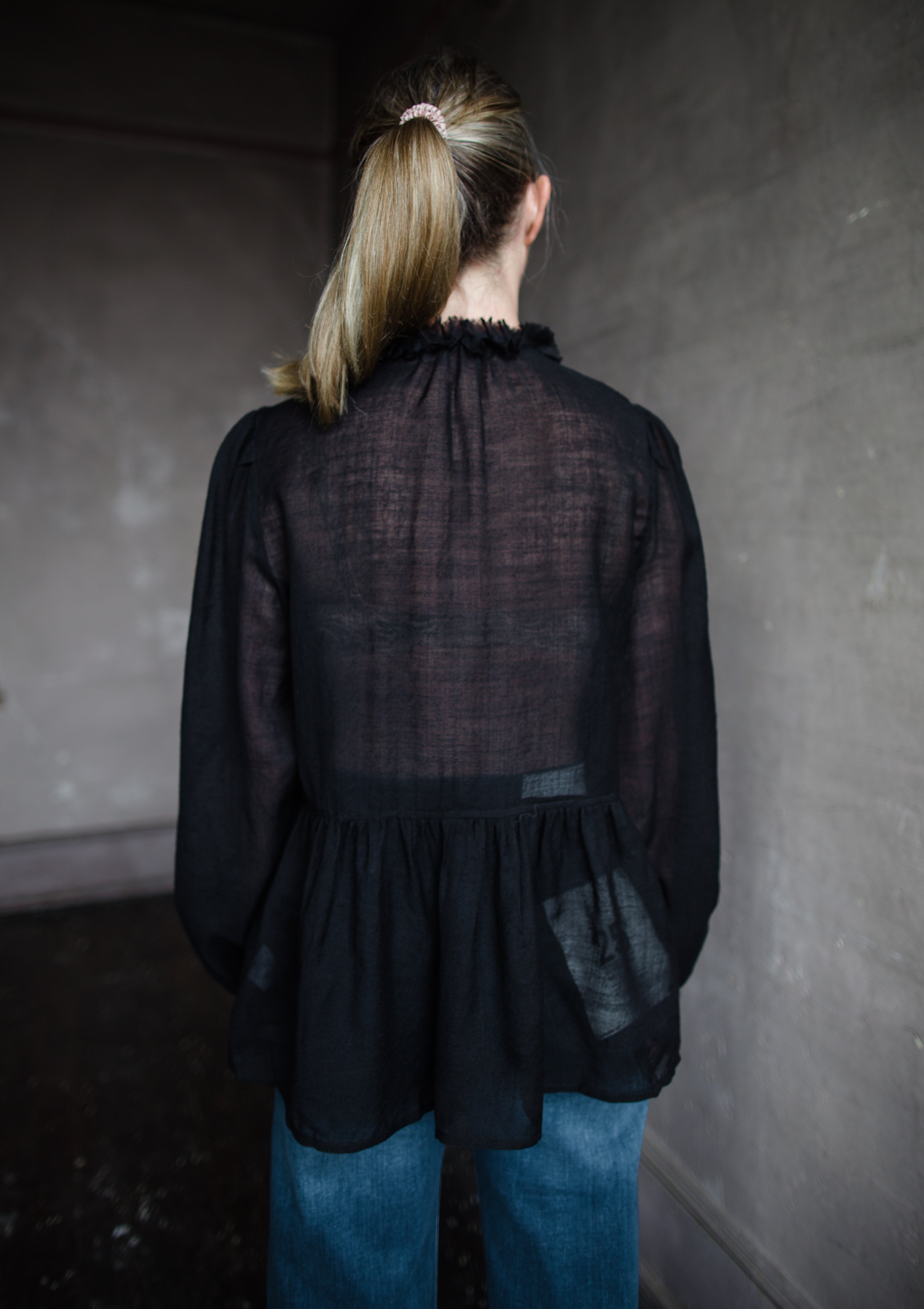 Image features woman wearing The Cosima Tunic by Ulla Johnson in Noir features a button down v neckline with rows of ruffles and iridescent sea shell buttons.