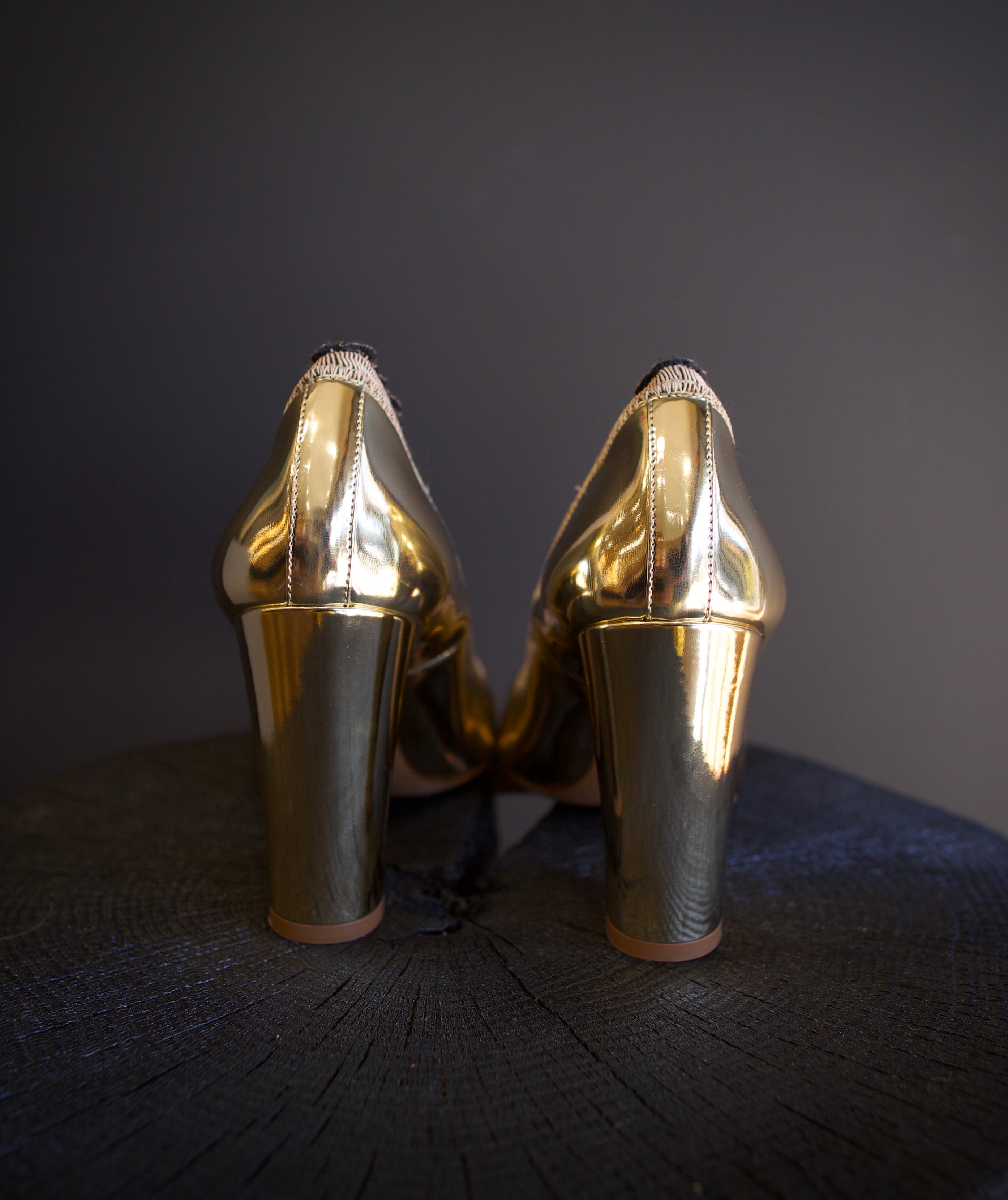 Image of the Elise Ruffle Pumps by Ulla Johnson feature a round toe and black tipped ruffle detailing in a polished gold color finish called platinum. 