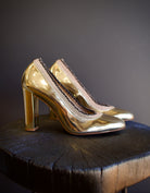 Image of the Elise Ruffle Pumps by Ulla Johnson feature a round toe and black tipped ruffle detailing in a polished gold color finish called platinum. 