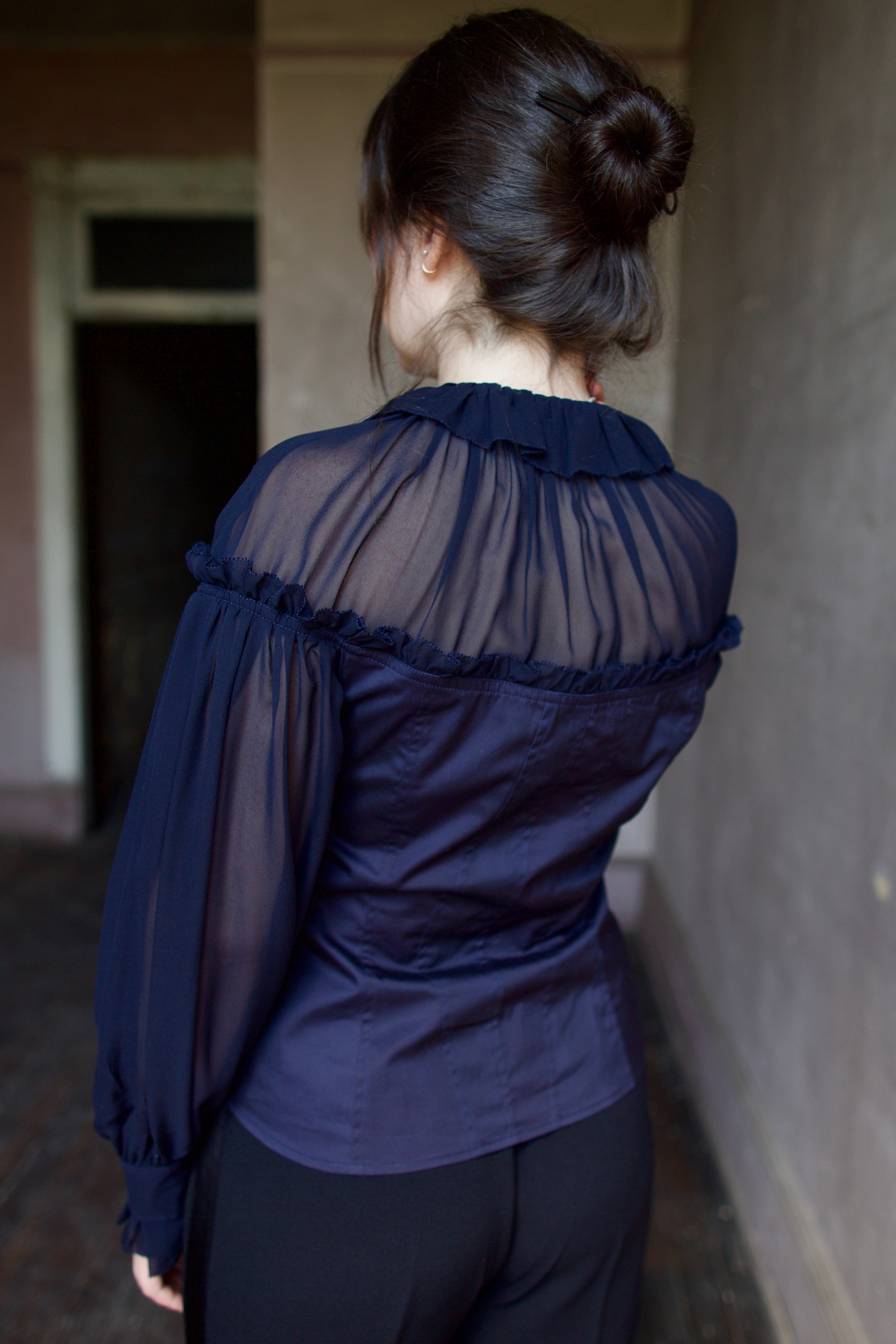 Back of model wearing a dark blue cotton and silk blouse with sheer long sleeves by designer Ulla Johnson