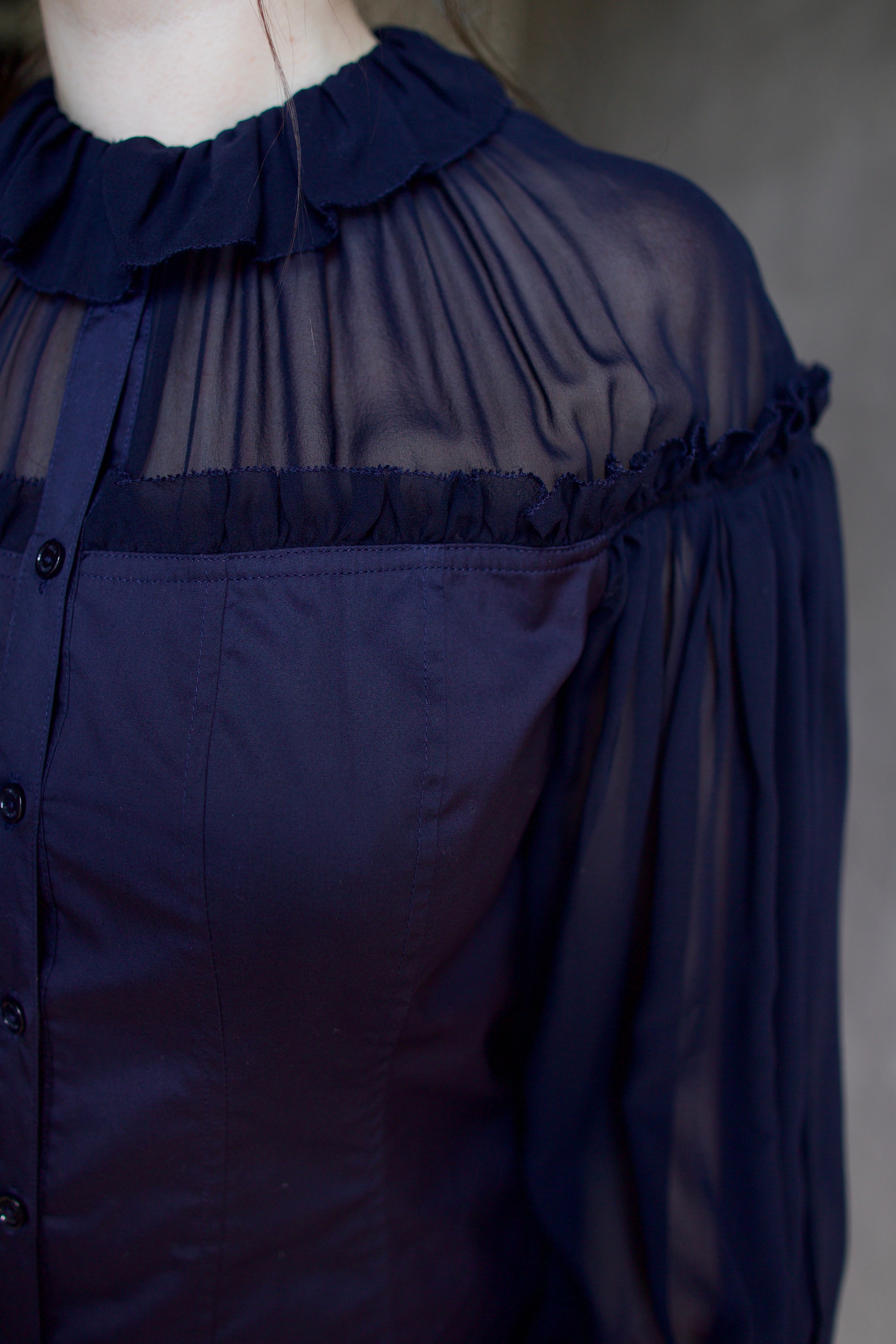 Detail photo of woman wearing a dark blue cotton and silk blouse with sheer long sleeves by designer Ulla Johnson