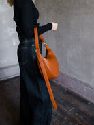 Image featuring a woman wearing the Twyla leather handbag by Ulla Johnson with a zip closure in a half moon shape and an adjustable strap in Sierra.