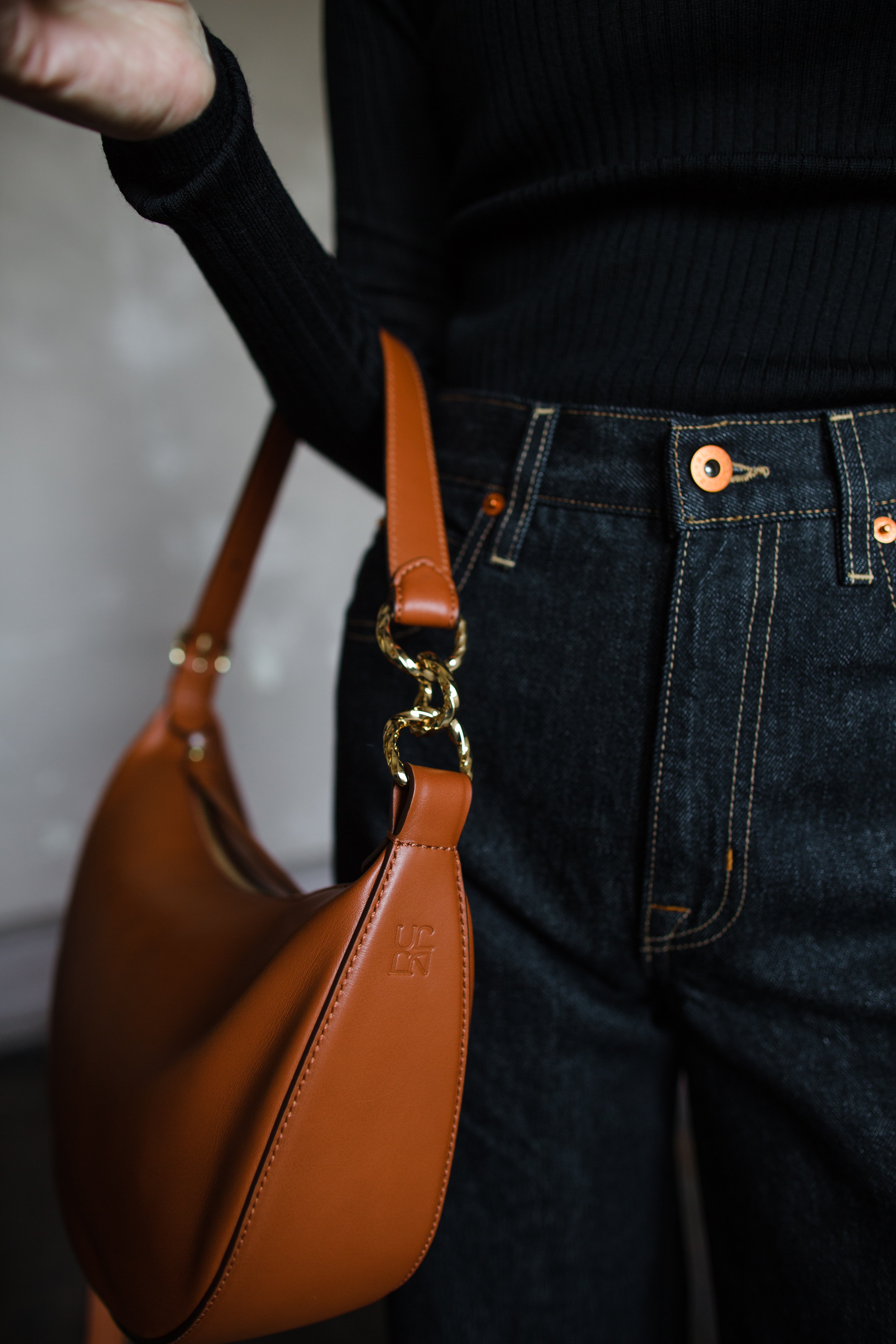 Image featuring a woman wearing the Twyla leather handbag by Ulla Johnson with a zip closure in a half moon shape and an adjustable strap in Sierra.