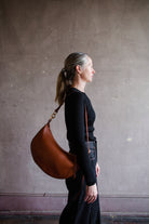 Image featuring a woman wearing the Twyla leather handbag by Ulla Johnson with a zip closure in a half moon shape and an adjustable strap in Sierra.