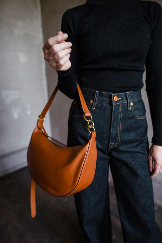 Image featuring a woman wearing the Twyla leather handbag by Ulla Johnson with a zip closure in a half moon shape and an adjustable strap in Sierra.