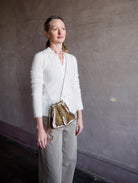 Image featuring a woman wearing the Adria wave pochette by Ulla Johnson with a drawstring closure, a crossbody strap and metal bangle in Platino gold.