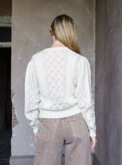 Image featuring a woman wearing the Haley sweater by Ulla Johnson with a slightly sheer weave, mother of pearl buttons and long sleeves in ivory alpaca.