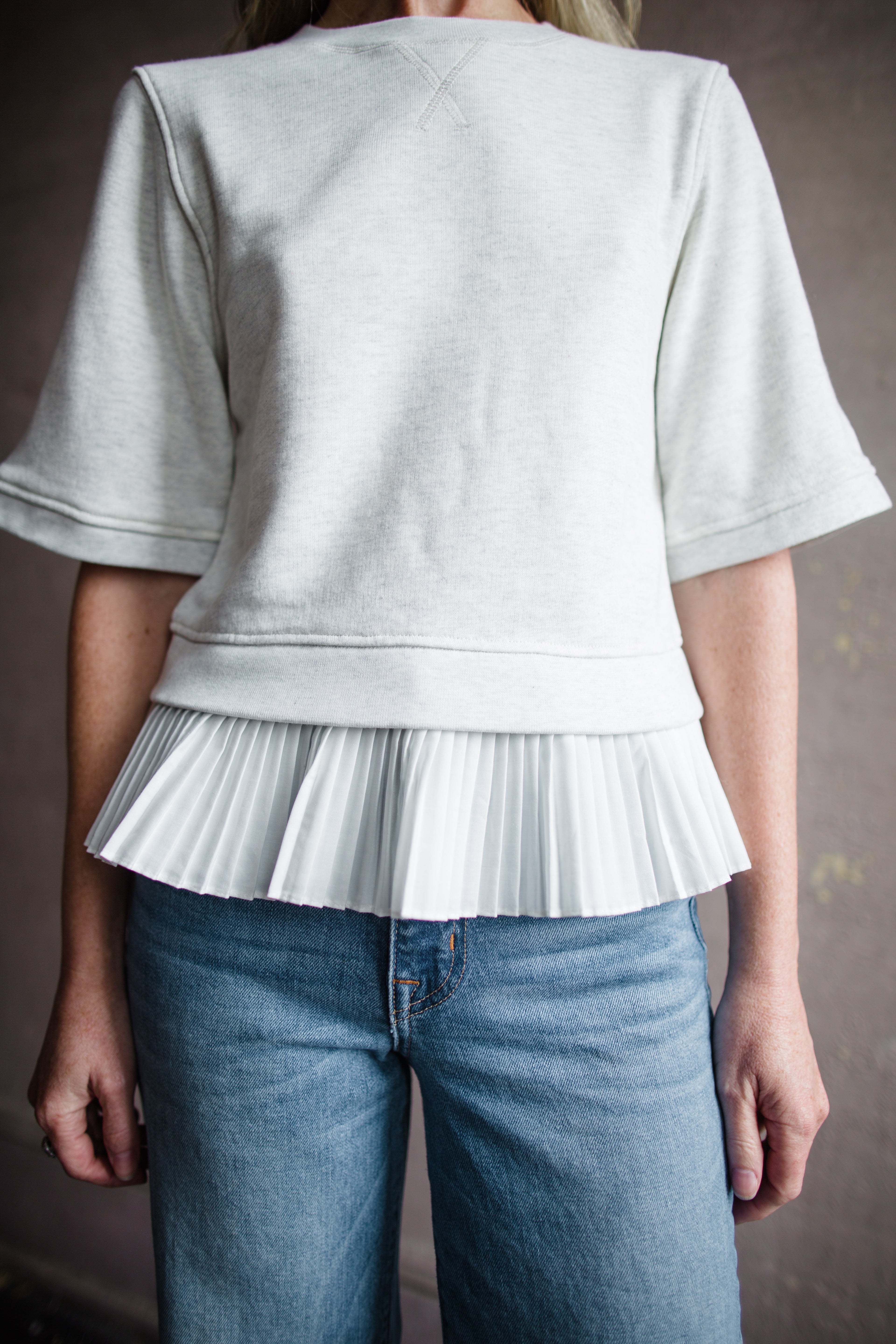 Mature woman wearing the Ulla Johnson Harper  Top grey short sleeve sweatshirt with layered white top 