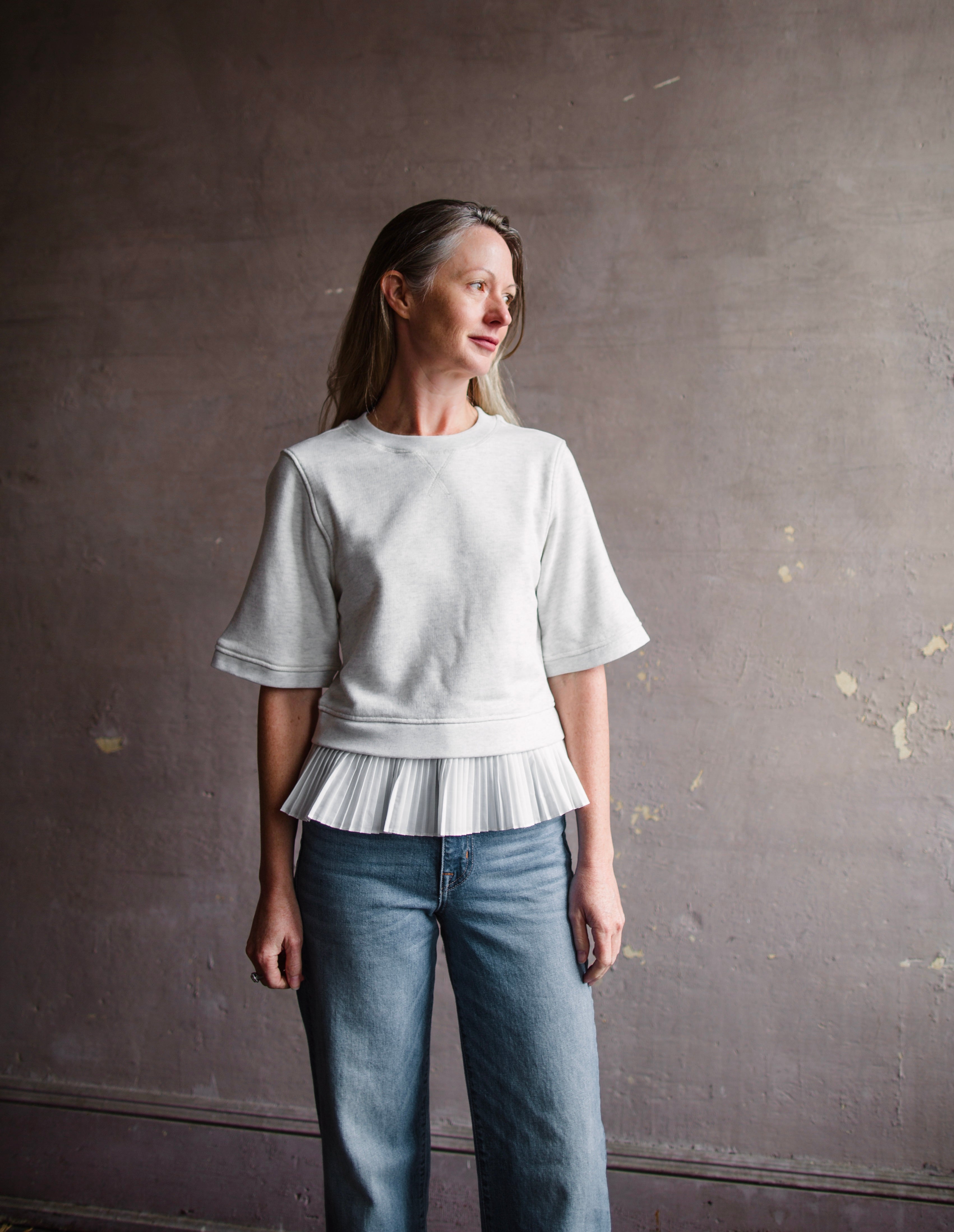 Mature woman wearing the Ulla Johnson Harper  Top grey short sleeve sweatshirt with layered white top 