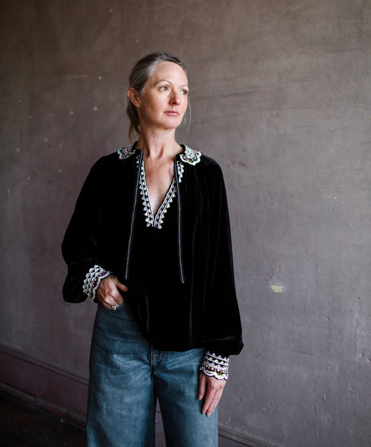 Image featuring a woman wearing the black velvet Julien top by Ulla Johnson with a split neckline, tie closure and embellished collar with sequins and beading.