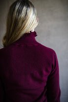 Image featuring a woman wearing the Maisie cashmere sweater by Ulla Johnson with a high neckline, drawstring detailing and a ribbed texture in burgundy.