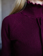 Image featuring a woman wearing the Maisie cashmere sweater by Ulla Johnson with a high neckline, drawstring detailing and a ribbed texture in burgundy.